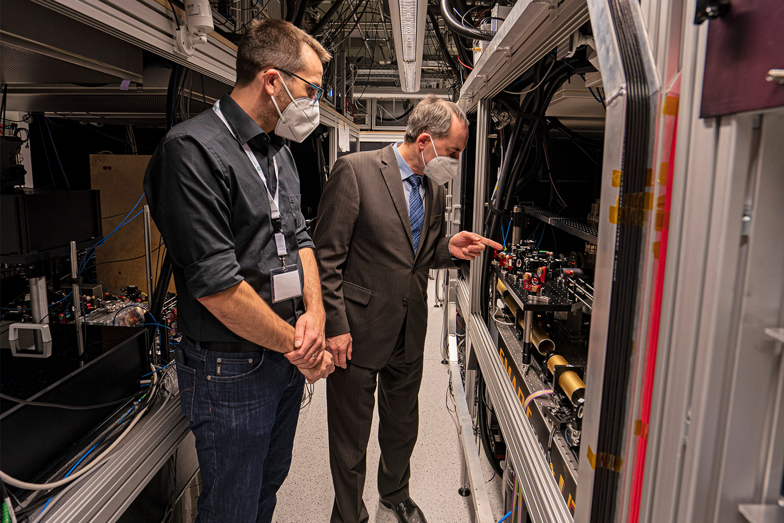 Sebastian Blatt, Forschungsleiter am MPQ und im Munich Quantum Valley (MQV), zeigt Minister Aiwanger einen der Quantensimulatoren am MPQ, aus dessen Technologie die WissenschaftlerInnen einen Quantencomputer basierend auf Neutralatomen bauen werden. 